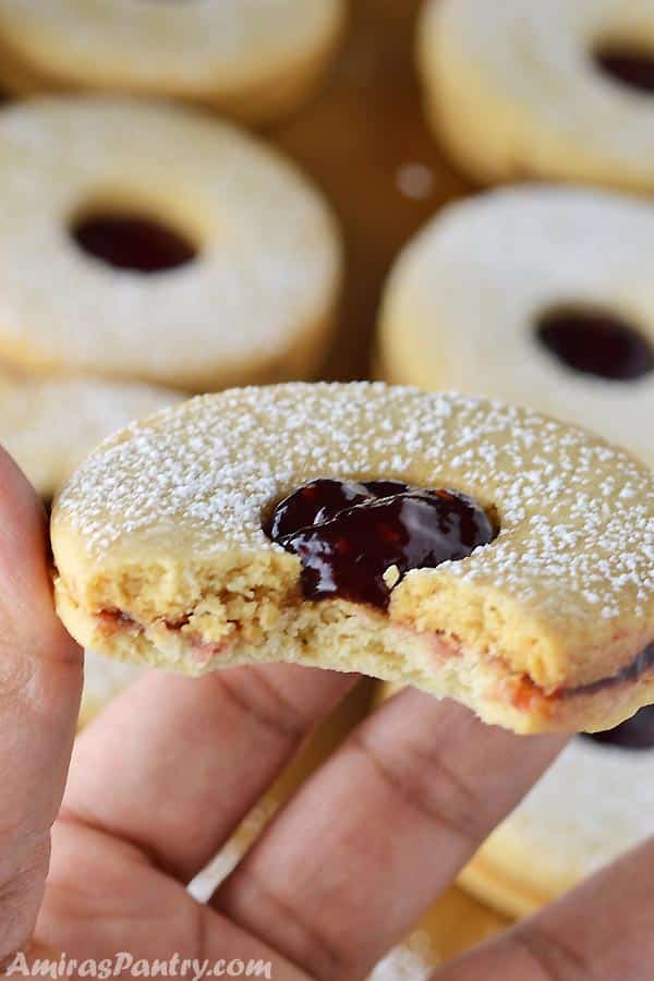 A hand holding a linzer cookie with one bite take from it.