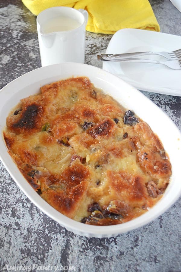 Om ali in a white deep oven dish with a small milk pitcher on the side and white plates.