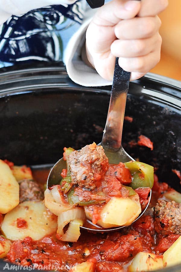 A child's hand holding a ladle and scooping some saucy meatballs from the slow cooker.