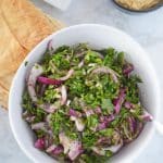 A white serving bowl with arugula salad with some pita bread on the side