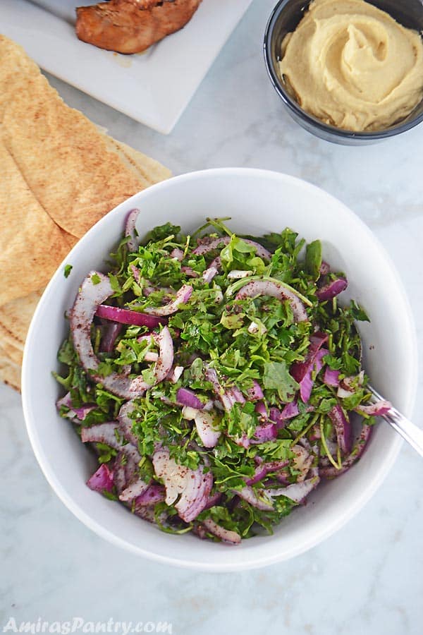 A white serving bowl with arugula salad with some pita bread on the side