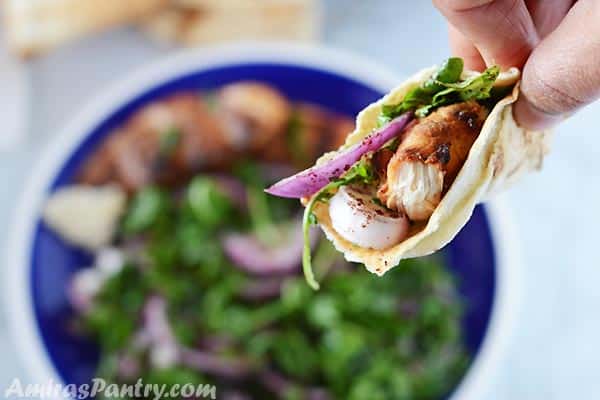 A hand holding a piece of pita bread with grilled chicken and arugula salad.