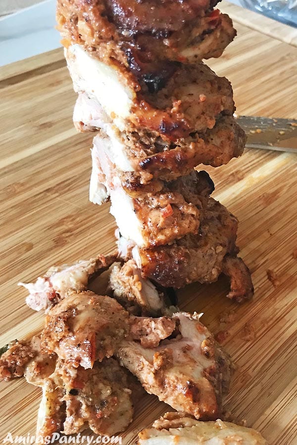 Layers of chicken on top of each others threadded on metal skewers and ready to be cut thin with some chicken thin slices on the board.