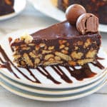 A white plate with a piece of Chocolate Biscuit Cake and touch of Chocolate Syrup decorating the plate