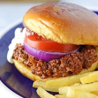 A sloppy joes sandwich placed on a blue plate with fries on the side.