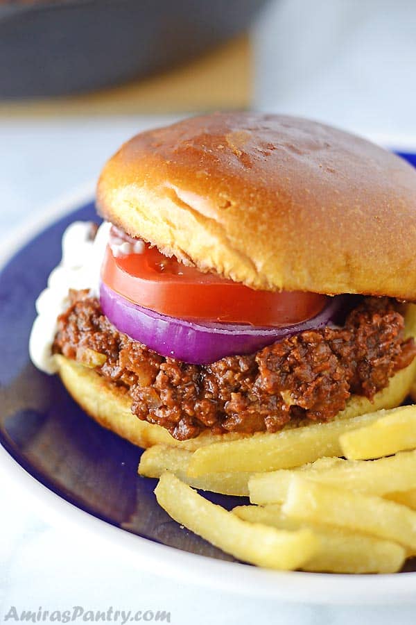 A sloppy joes sandwich placed on a blue plate with fries on the side.