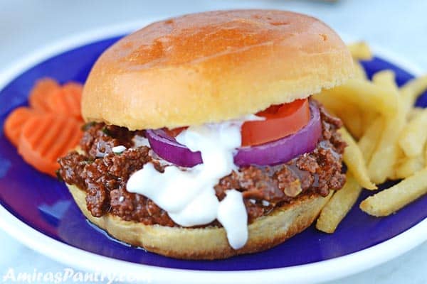 A shawarma spiced sloppy joes sandwich with white shawarma sauce dripping and showing tomato and onion rings in the sandwich.