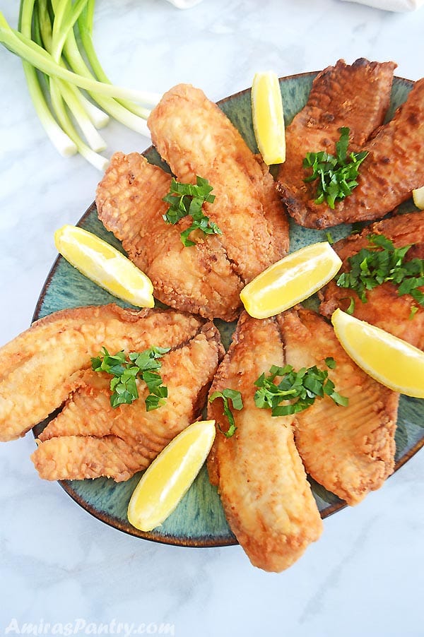 Fried tilapia fillets on a green oval serving platter with lemon wedges.