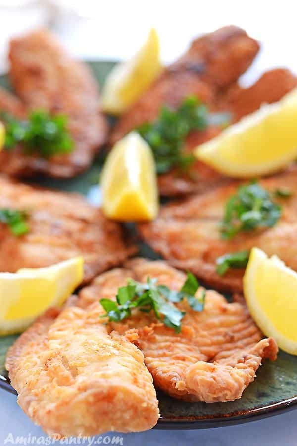 Tilapia fillets on a green platter decorated with lemon wedges and chopped parsley.