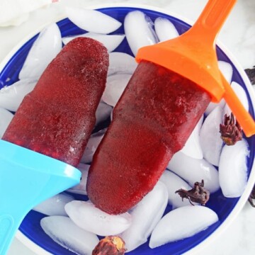 Two hibiscus popsicles on a blue plate full of ice.