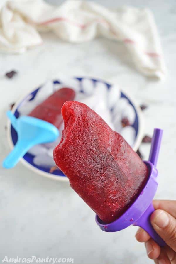 A hand holding one hibiscus popsicle with a bite taken from it.