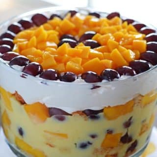 A big bowl of fruit trifle with mango pieces and grapes covering the top