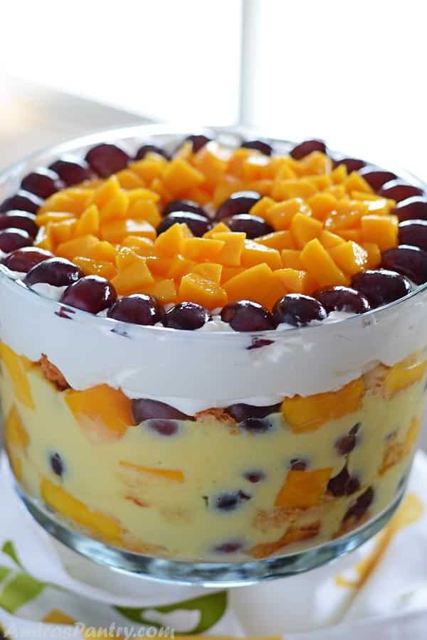 A big bowl of fruit trifle with mango pieces and grapes covering the top