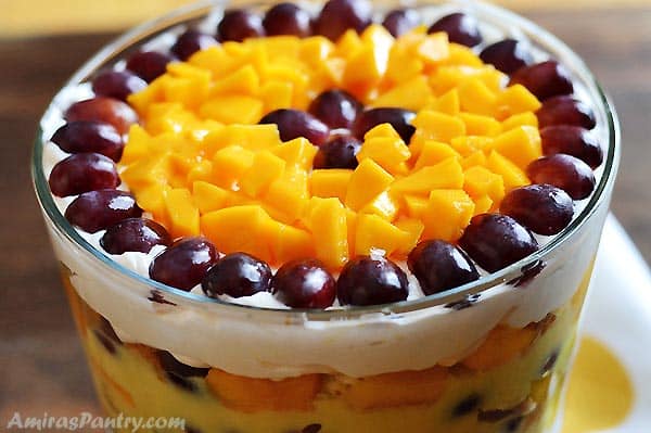 A trifle bowl with its top garnished with grape halves and diced mangoes. 