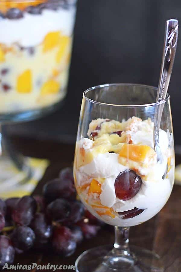 A glass of fruit trifle with a spoon in it.