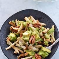 A black plate with avocado chicken salad on it with the whole serving bowl in the back.