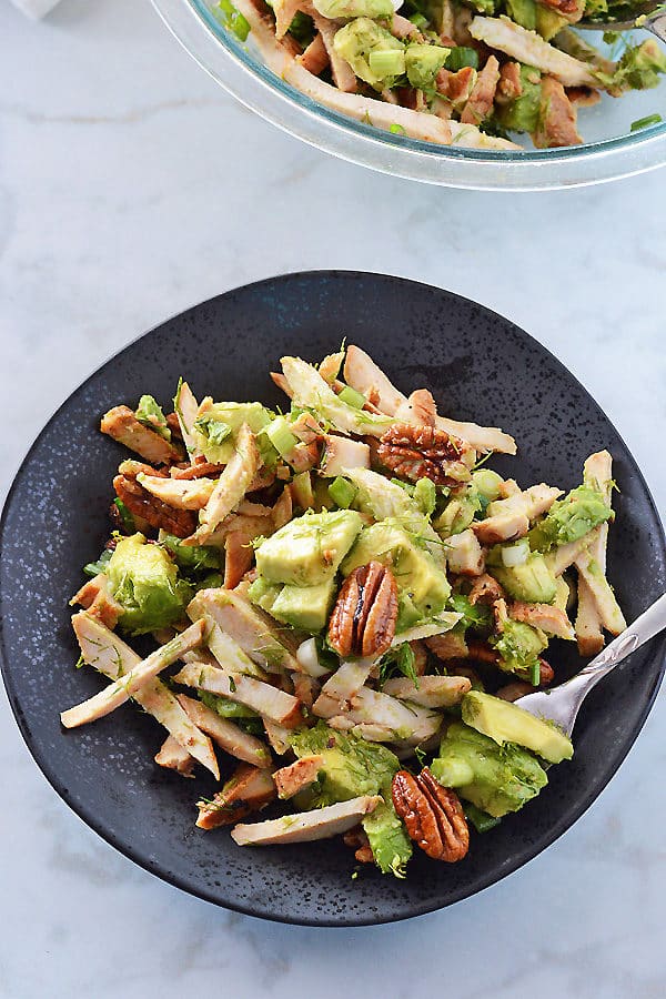 A black plate with avocado chicken salad on it with the whole serving bowl in the back.