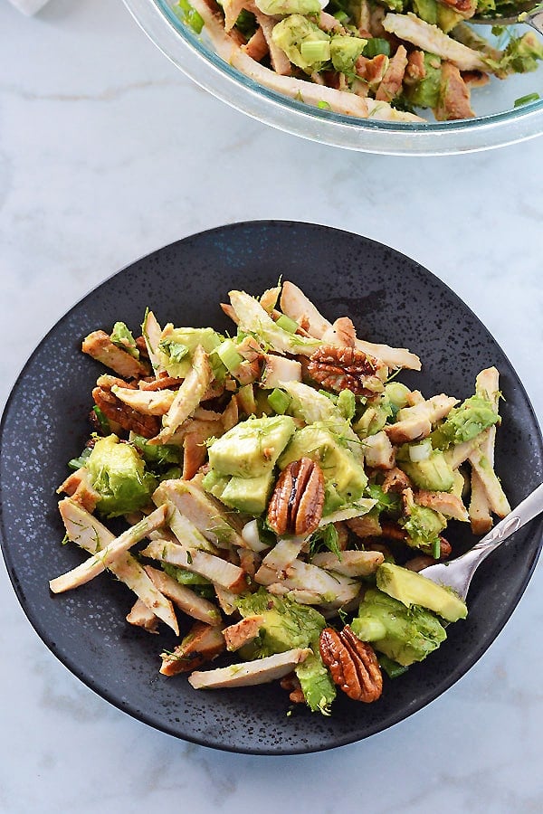 A black plate with avocado chicken salad on it with the whole serving bowl in the back.