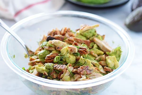 A big serving bowl of avocado chicken salad with a spoon in it.