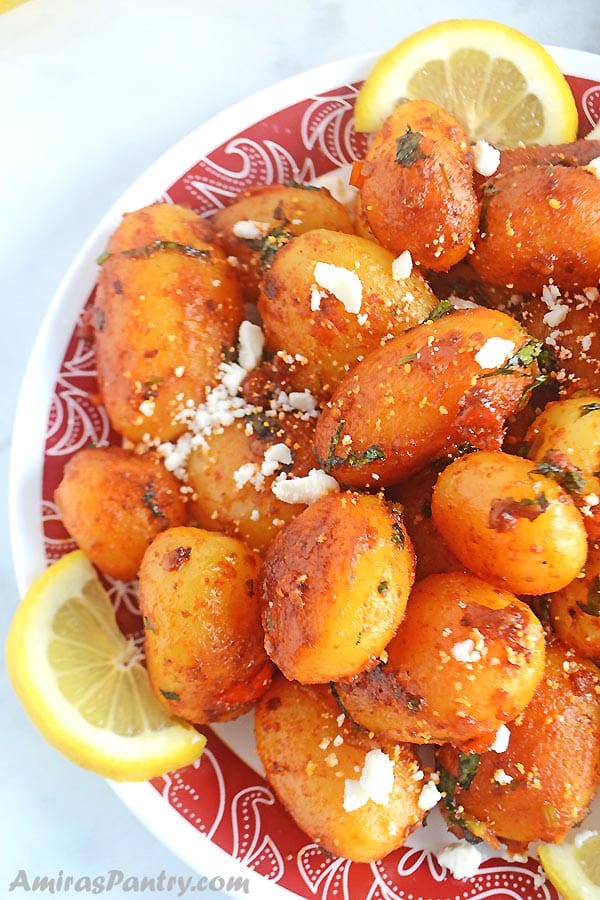 A white plate with a red rim of spicy potato salad with lemon rinds.