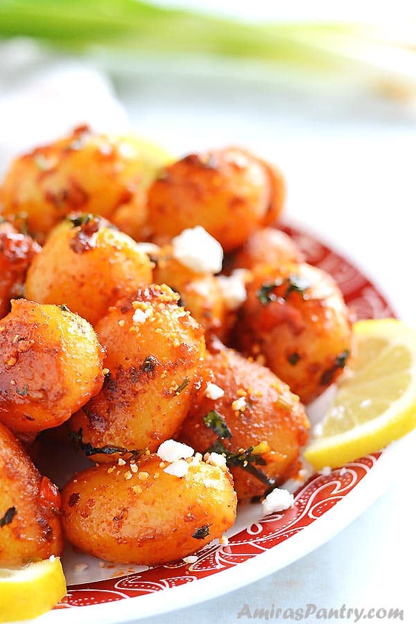 A white plate filled with spicy potato salad sprinkled with feta cheese and lemon rinds.