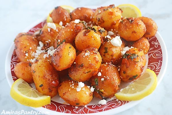 A white plate filled with spicy potato salad sprinkled with feta cheese and lemon rinds.