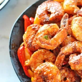 A black plate with shrimp fajitas on a bed of sauteed onions and bell peppers.