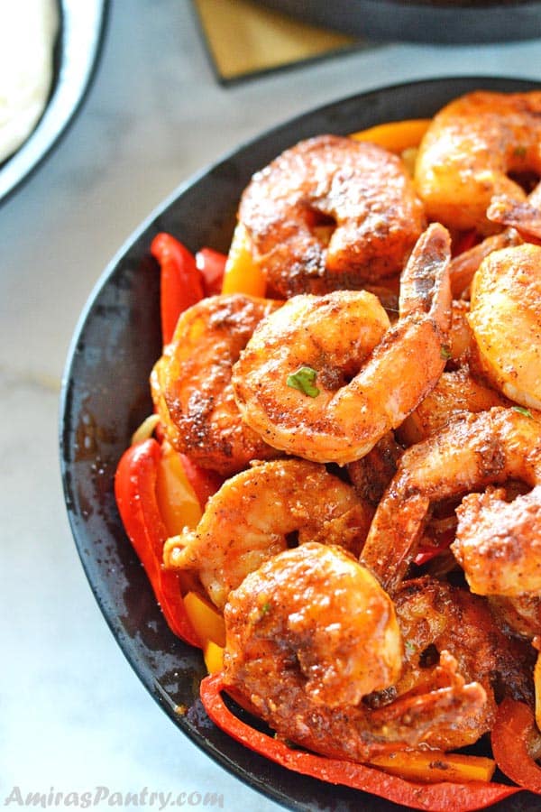 A black plate with shrimp fajitas on a bed of sauteed onions and bell peppers.