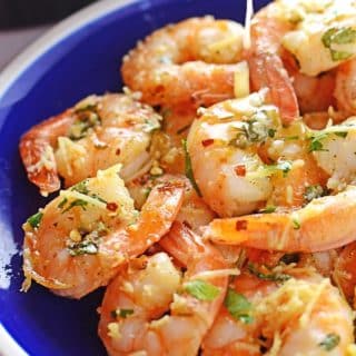 shrimp scampi on a blue plate with a spoon pouring some scampi sauce on top.