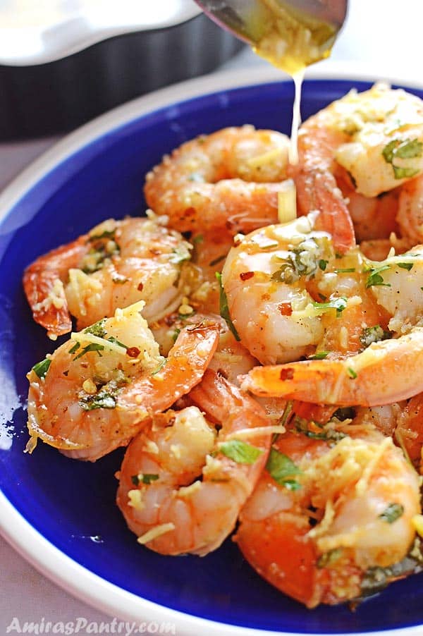 shrimp scampi on a blue plate with a spoon pouring some scampi sauce on top.