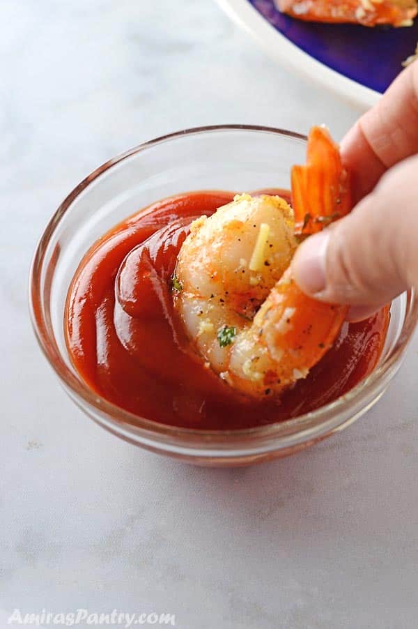 A hand dipping one shrimp in red sauce.