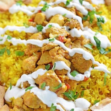 Yellow rice topped with chicken shawarma pieces and toasted bread in a platter and topped with shawarma white sauce.