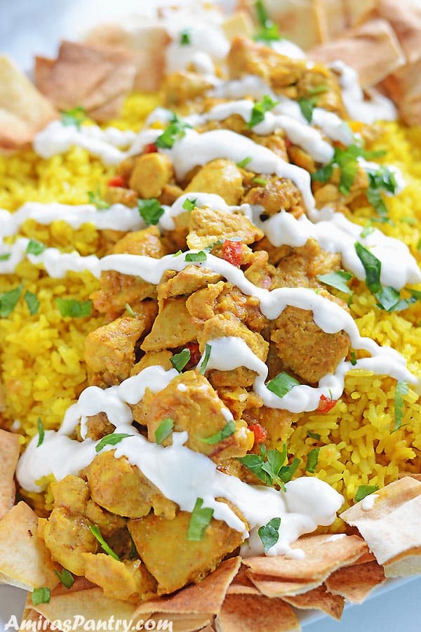 Yellow rice topped with chicken shawarma pieces and toasted bread in a platter and topped with shawarma white sauce.