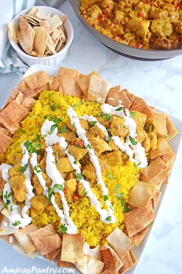 A white square platter with yellow rice and chicken shawarma with some toasted pita bread on the side.