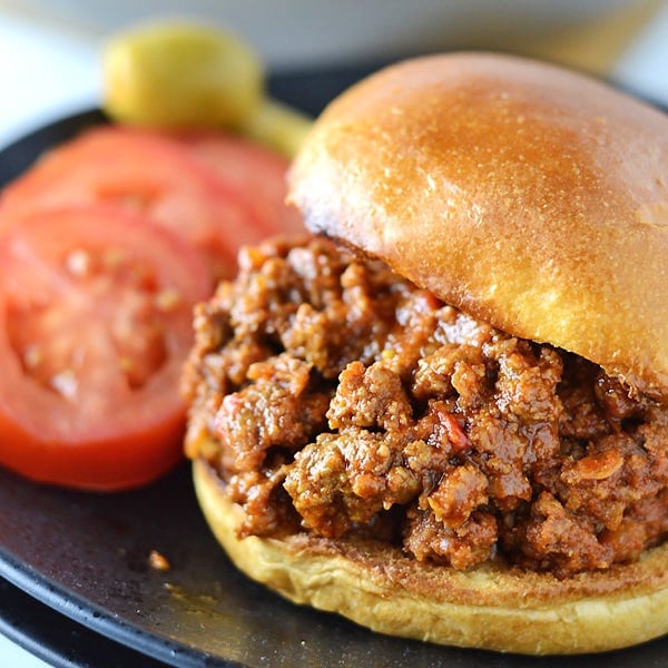 A close up image of sloppy joes sandwich with tomato slices on the back.