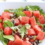 A white plate with watermelon and feta salas, some pita bread pieces are visible on the background