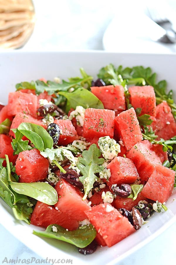 A white plate with watermelon and feta salas, some pita bread pieces are visible on the background