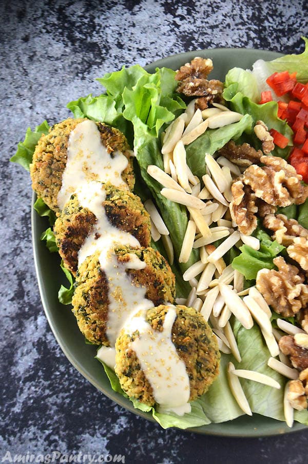 A green plate with baked flafel drizzled with some tahini sauce. Some lettuce and almonds on the plate as well.