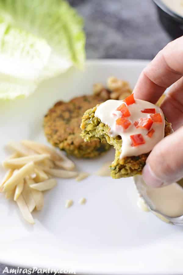 A hand holding one falafel patty covered with tahini sauce and some red bell pepper.