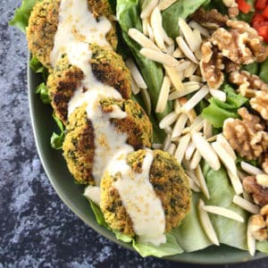 A green plate of baked falafel drizzled with tahini sauce with some lettuce and nuts on the plate.