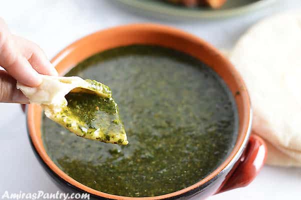 A hand scooping some molokhia soup with a piece of pita bread