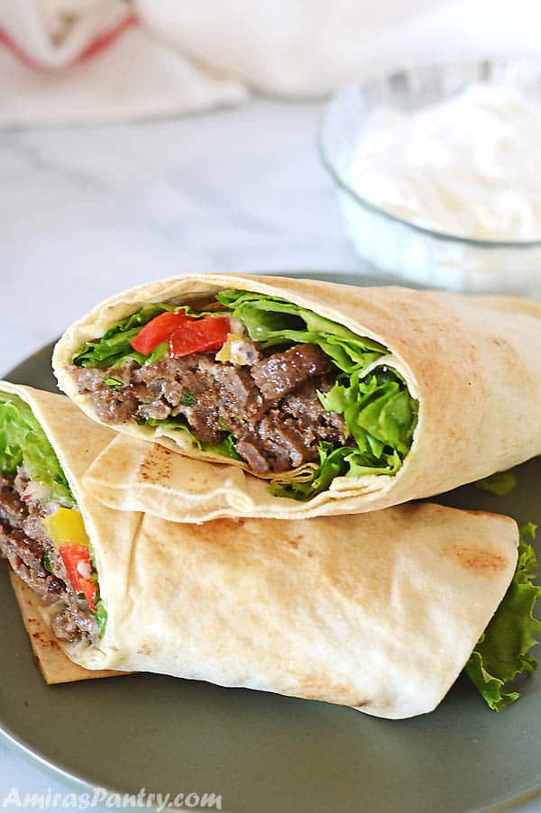 Beef Shawarma wrap on a dark green plate with a bowl of white shawarma sauce on the back.