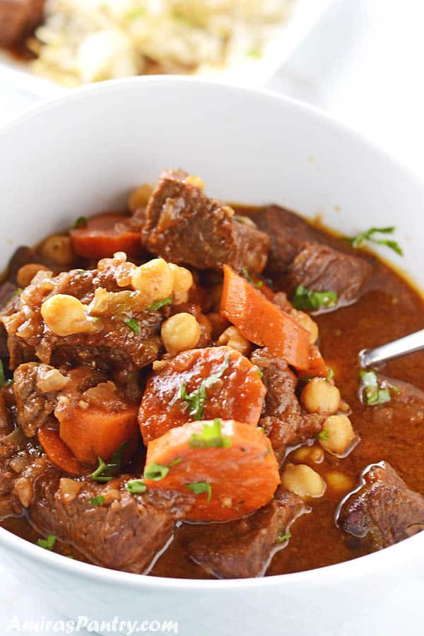 Beef stew in a white bowl with carrots and chickpeas and garnished with some chopped parsley