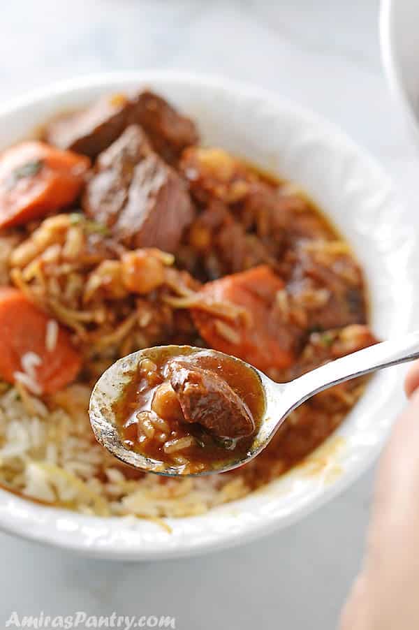 A spoon scooping some beef stew and rice from a white plate on the table.
