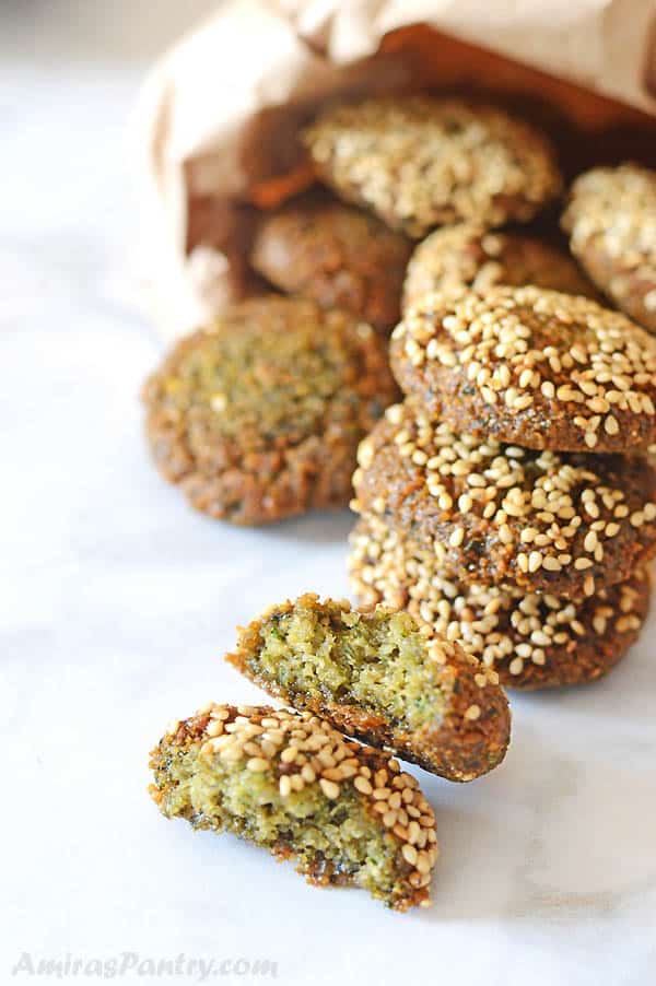 falafel patties in a borwn bag with some patties on a white marble table and one falafe is cut in halves to show texture.