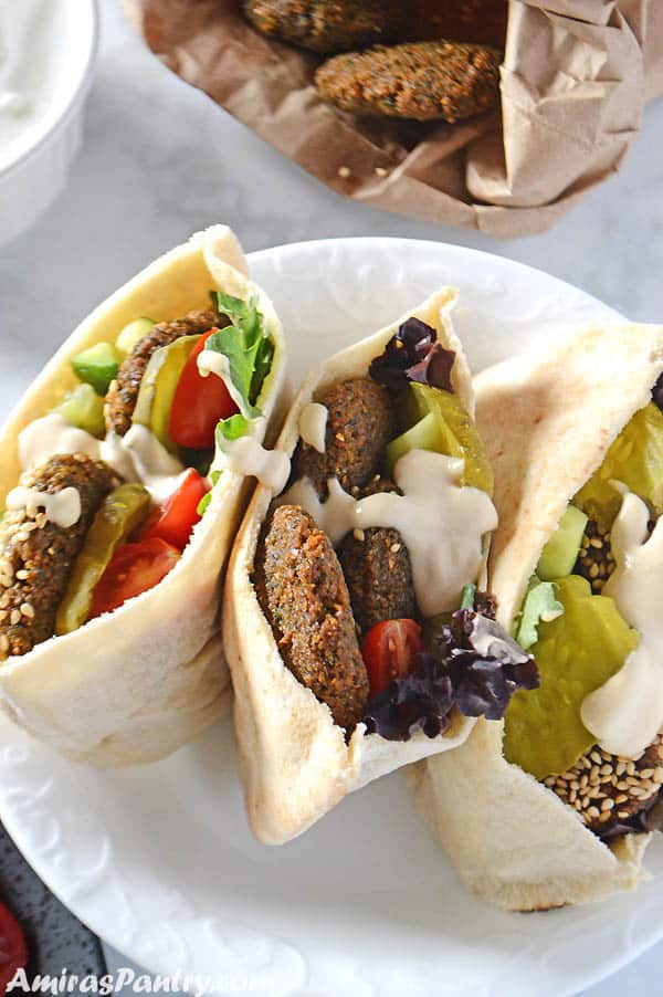 falafel sandwiches on a ahite plate and filled with greens with a drizzle of tahini sauce.