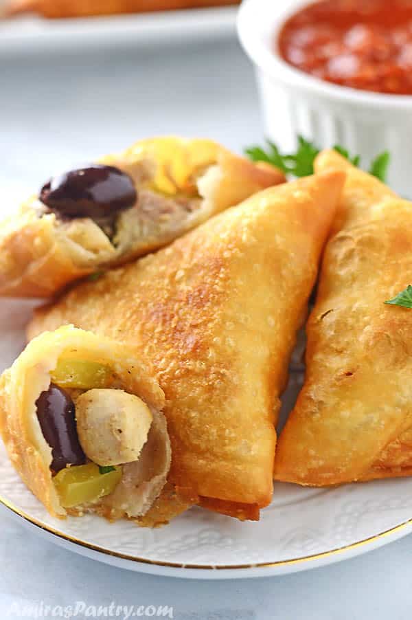 Chicken samosas cut in half to show filling place on a white table.
