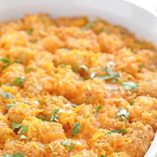 Tatter tots casserole in a white oven dish on a white table and garnished with parsley