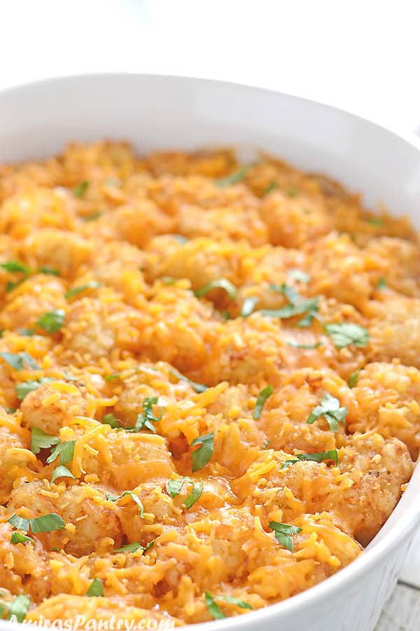 Tatter tots casserole in a white oven dish on a white table and garnished with parsley