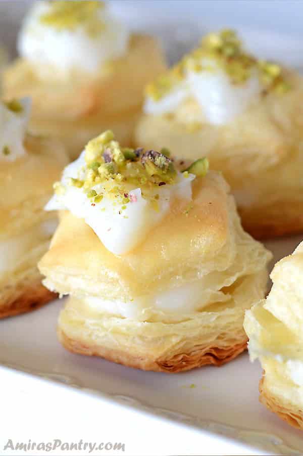 Shaabiyat stuffed and topped with cream and garnished with pistachios on a white plate.